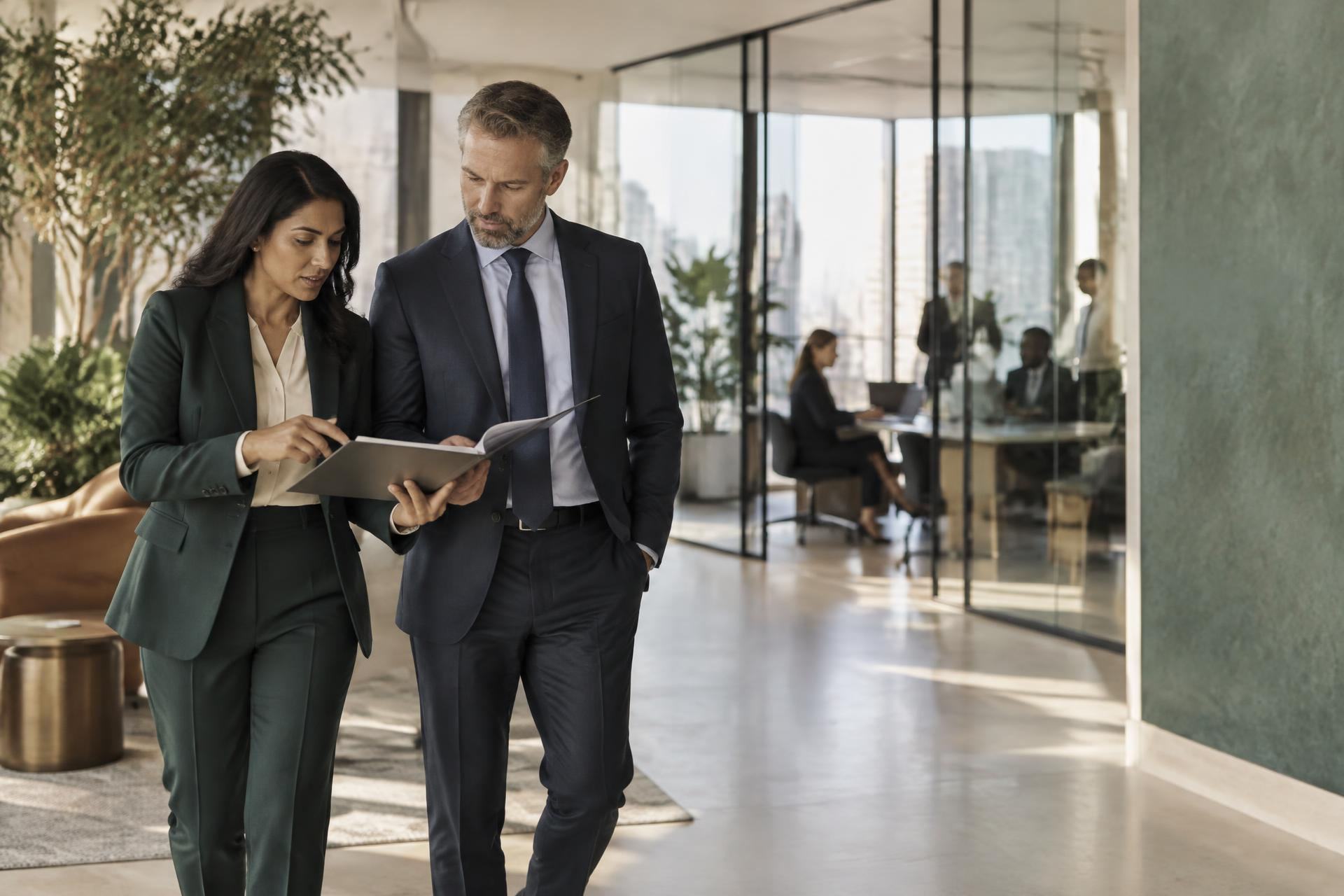 Two senior professionals reviewing a document while walking through a bright workplace